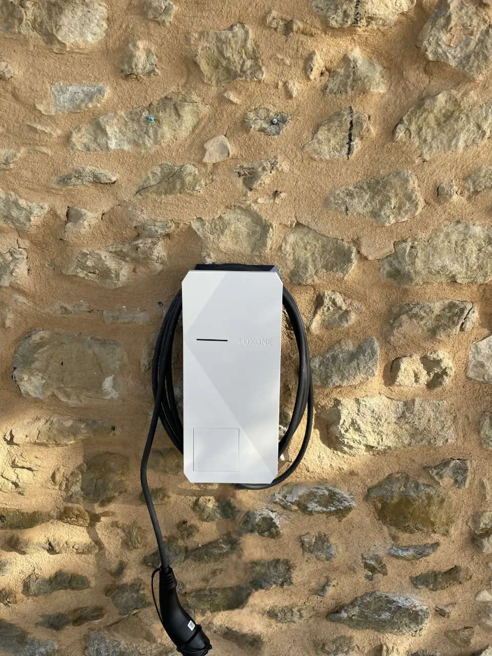 Borne de recharge Loxone Wallbox installée sur un mur en pierre, câble de charge enroulé