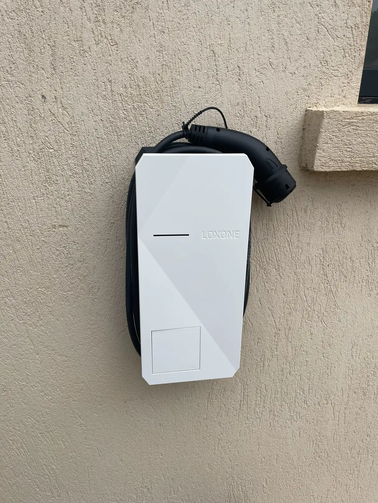Wallbox Loxone installée en façade, câble de charge et connecteur Type 2 rangés sur le support