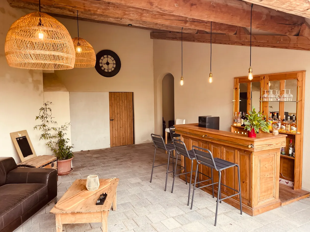 Pièce de vie aux poutres apparentes éclairée par des suspensions en rotin et des ampoules nues au-dessus d'un bar en bois