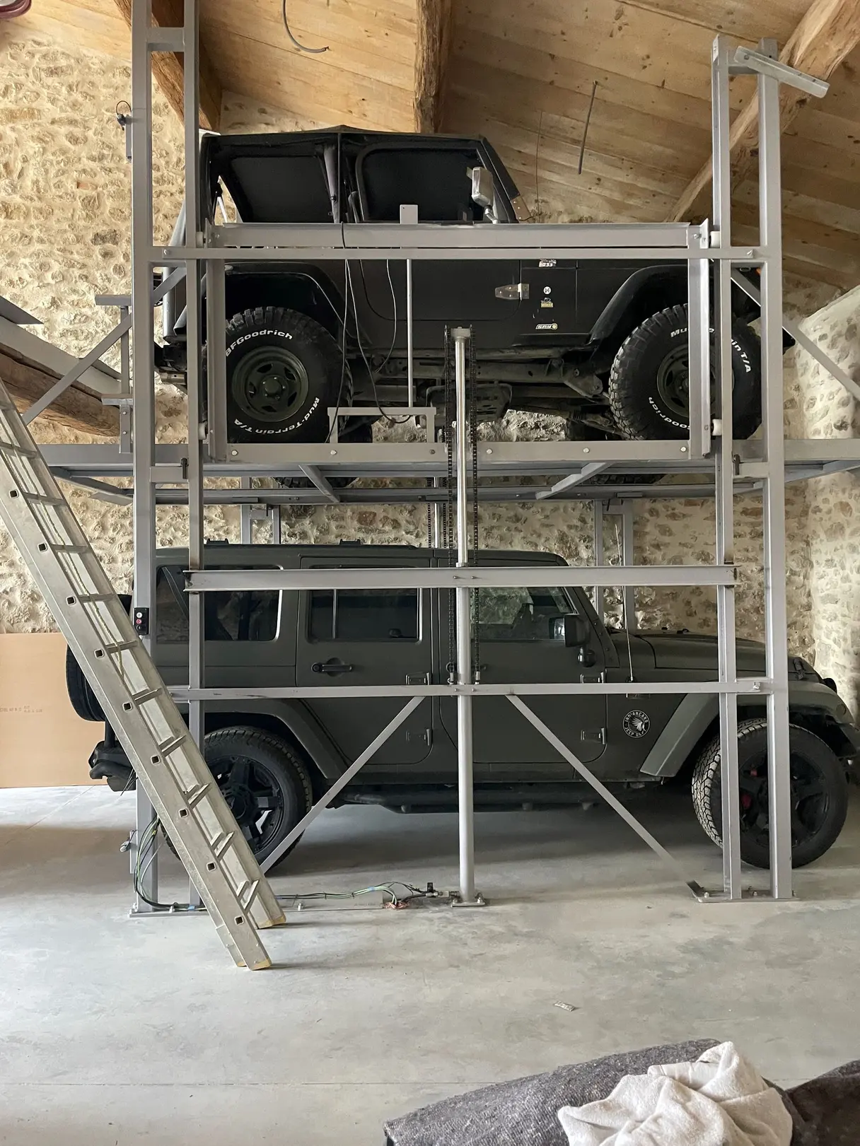 Élévateur à voiture superposant deux 4x4 dans un garage aux murs de pierre et charpente apparente