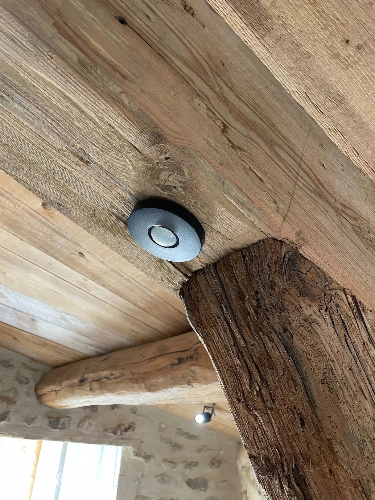 Détecteur de présence Loxone encastré dans le plafond en bois, près d'une poutre ancienne