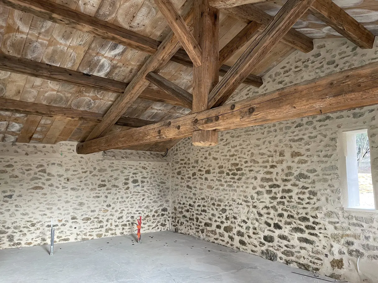 Volume du garage avant travaux : charpente apparente, murs en pierre et sol béton