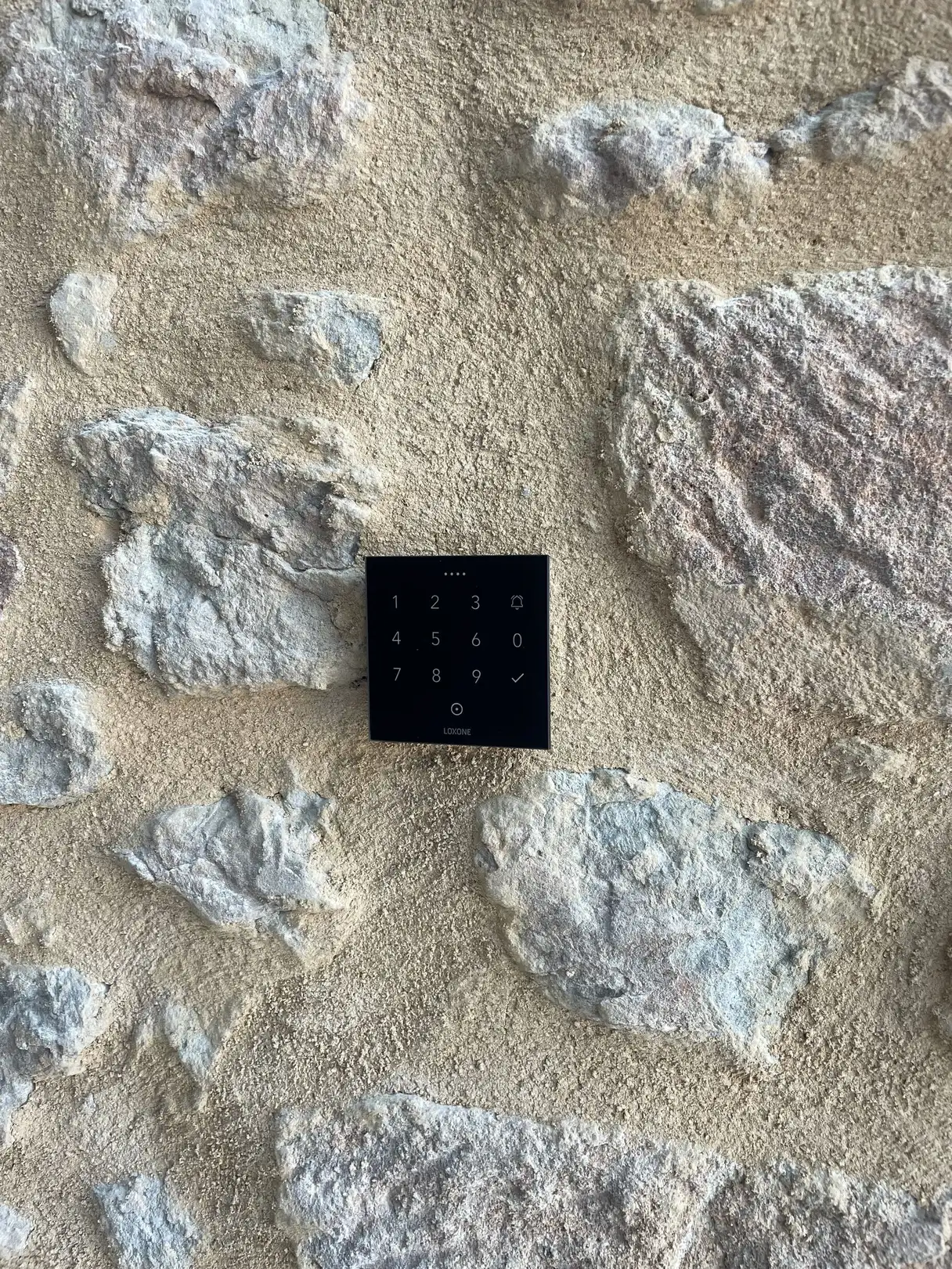 Clavier à code Loxone encastré dans le mur en pierre à l'entrée du garage