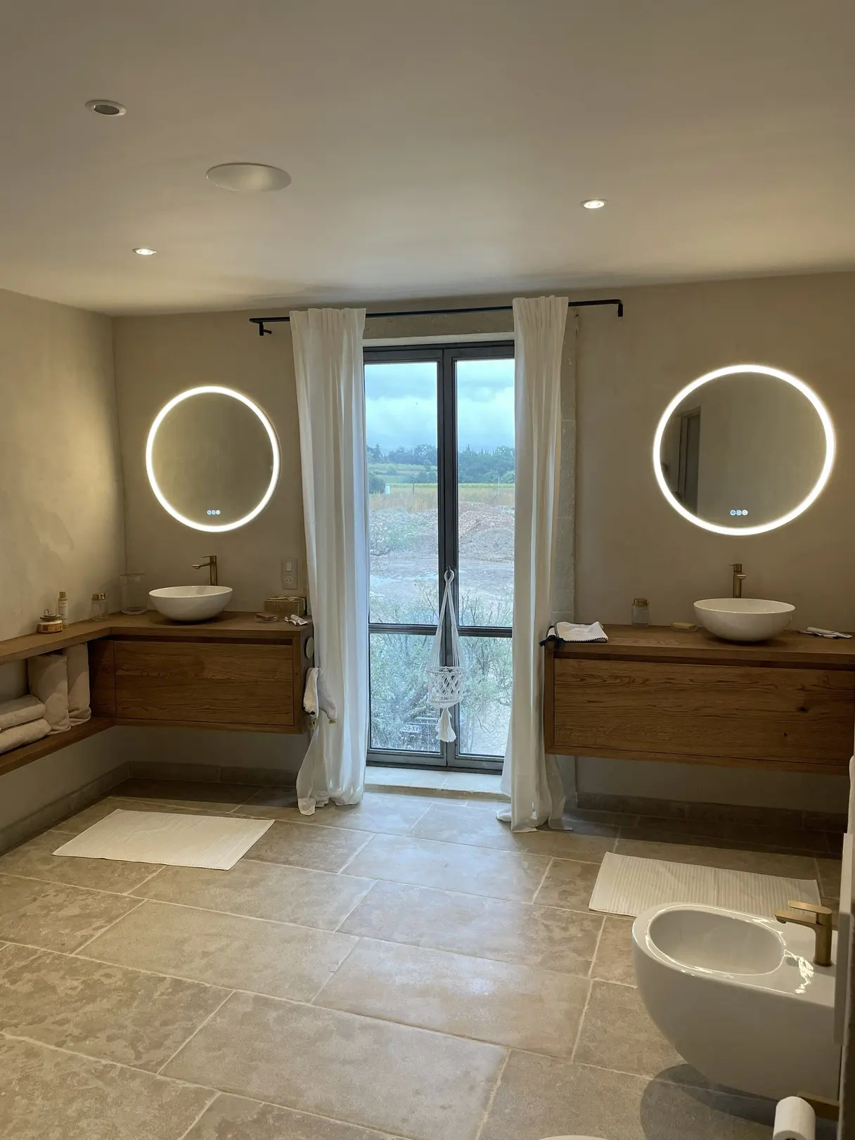 Salle de bains du mas : deux vasques, miroirs ronds rétroéclairés et éclairage encastré piloté