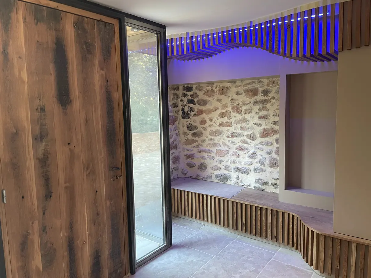 Entrée du mas : porte en bois massif, banquette en tasseaux et éclairage d'ambiance bleu intégré