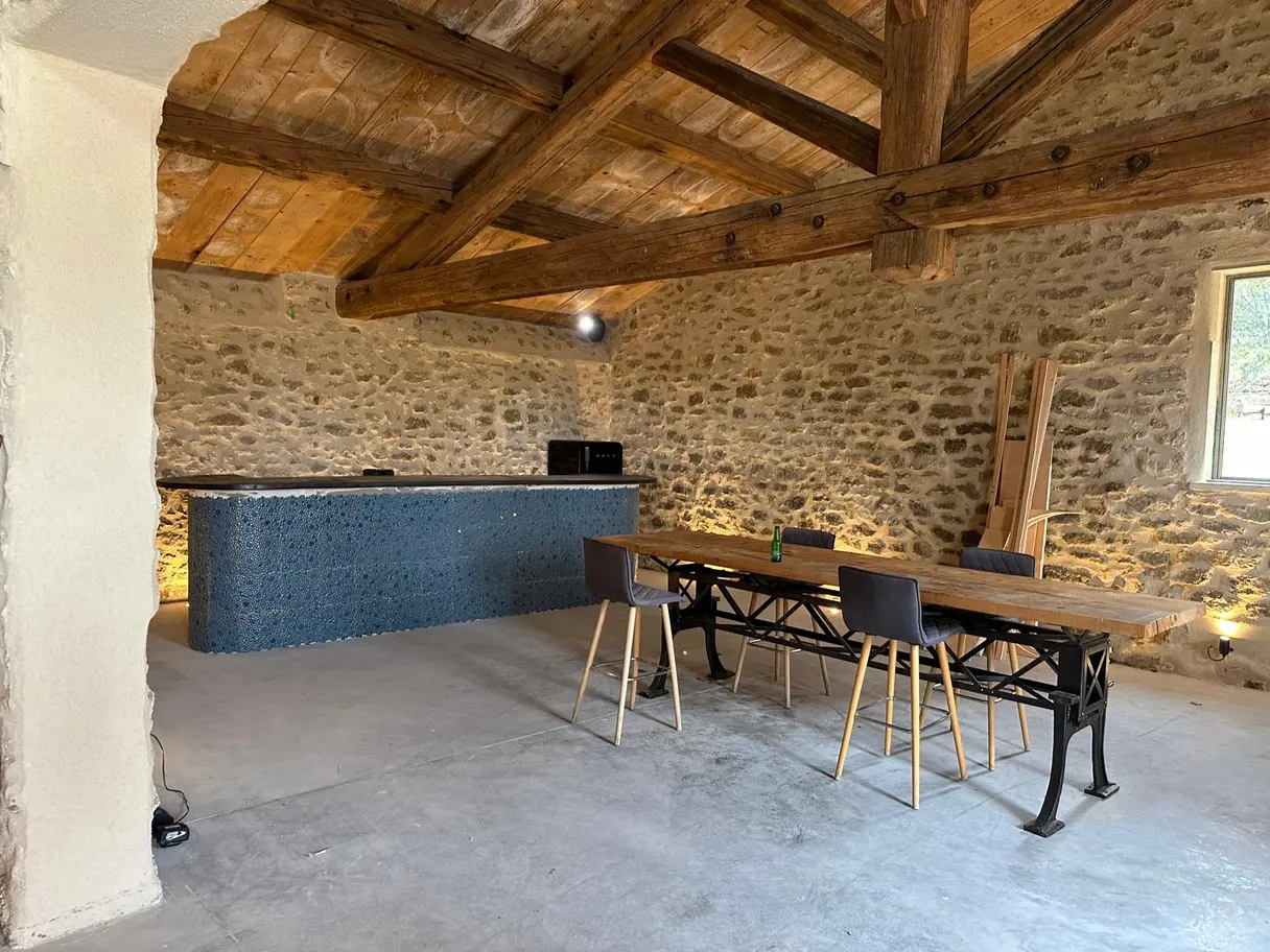 Salle à manger sous charpente : grande table, îlot en pierre et éclairage scénarisé