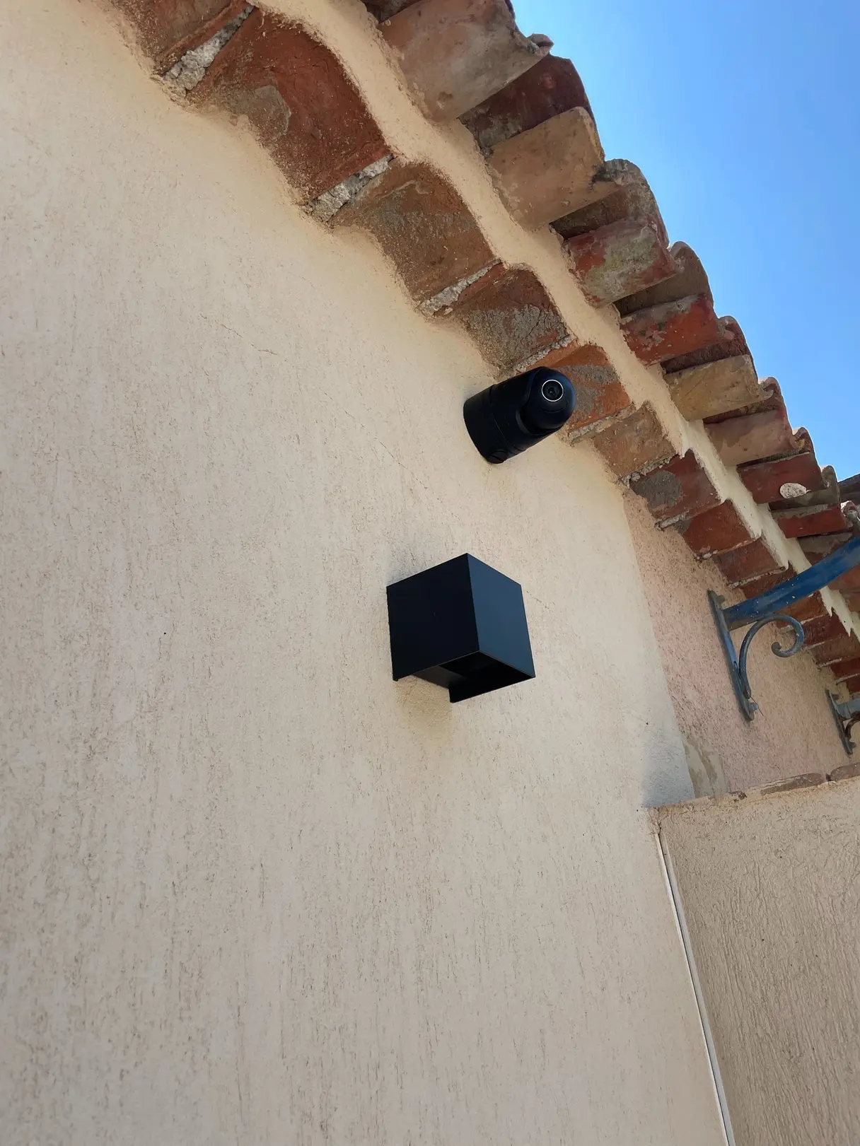 Caméra et applique extérieure installées sous la génoise d'une maison en pierre
